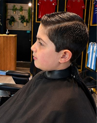 Corte infantil desde el perfil en silla de barbería
